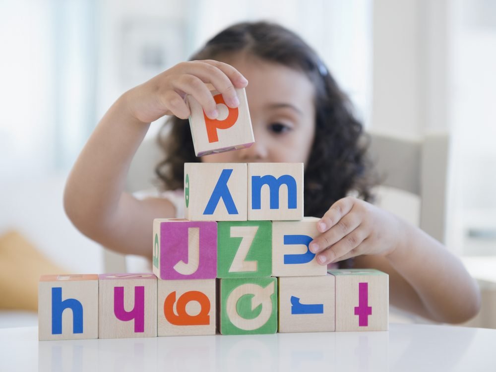 A young child stacking coloured alphabet blocks