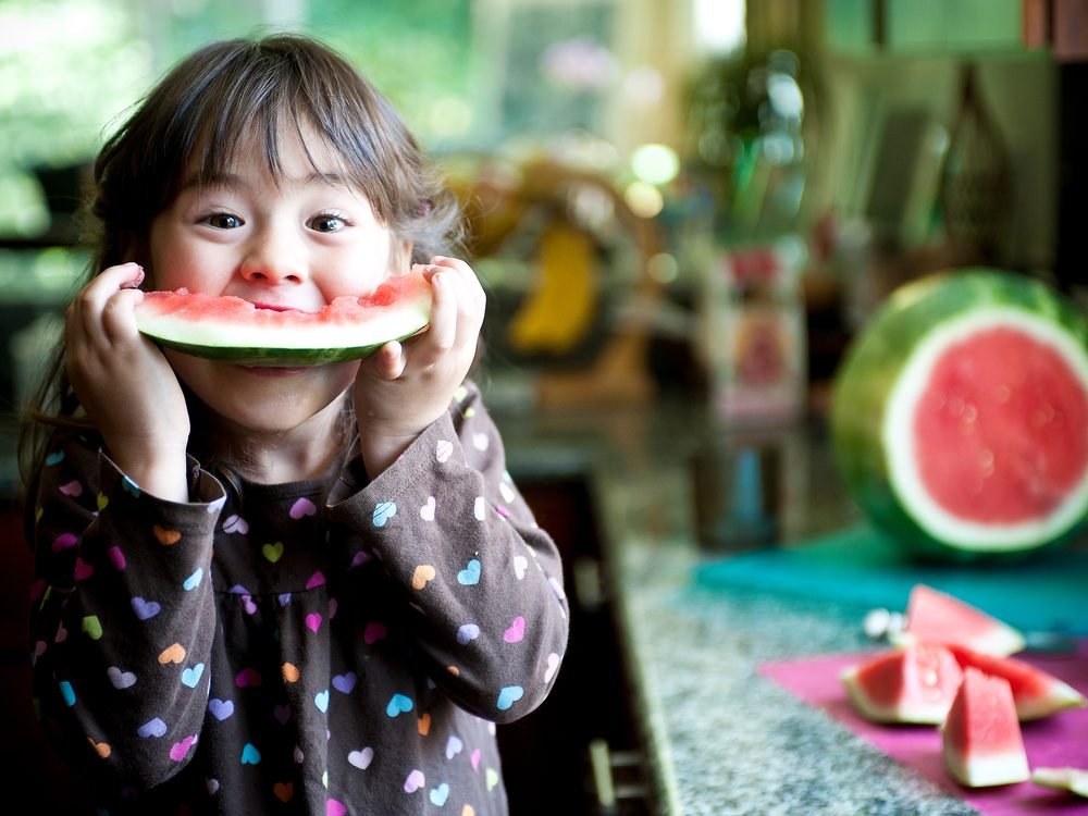 A child smiling while eating a slice of watermelon